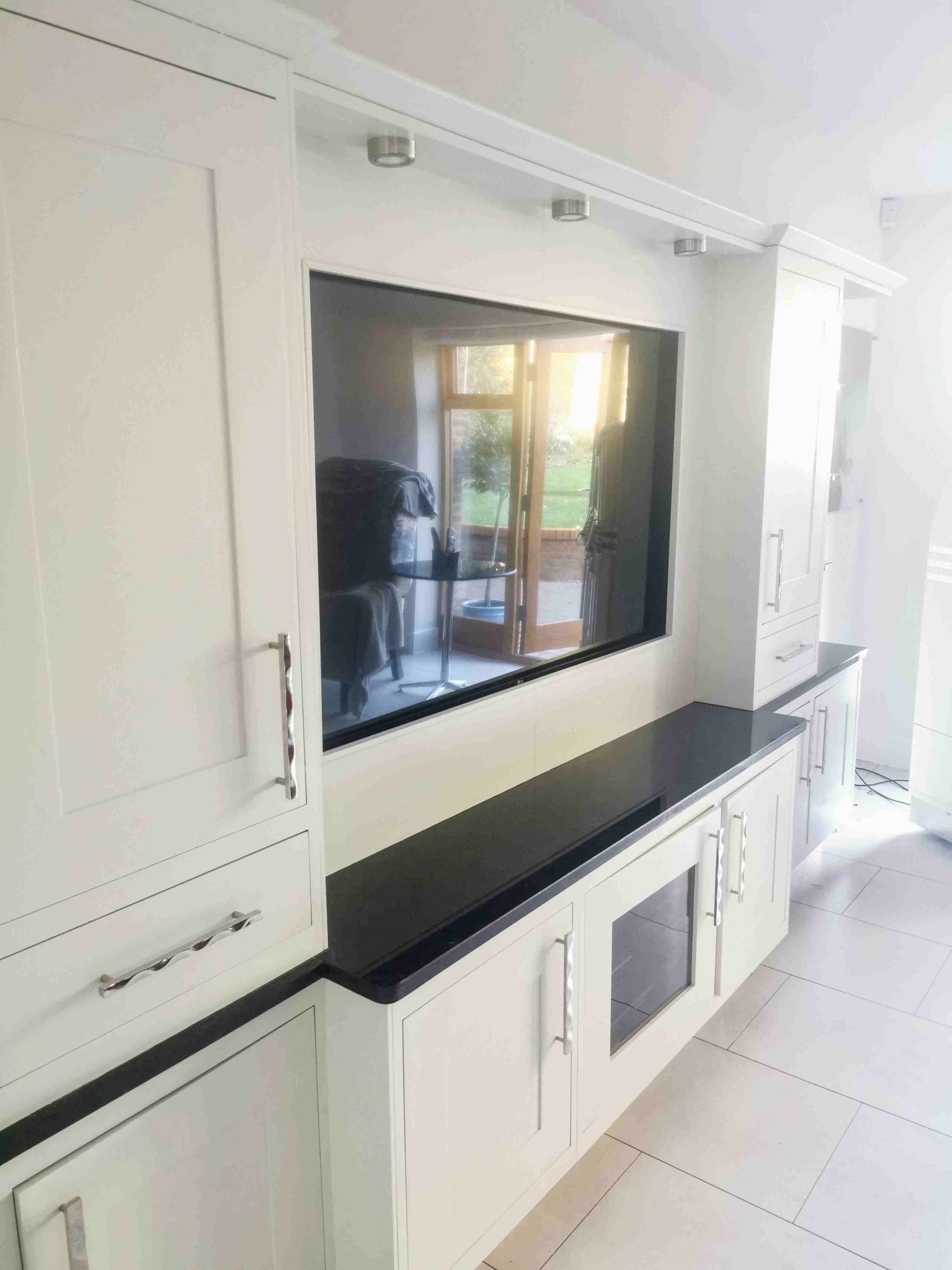 White painted kitchen units built around a wall-mounted television